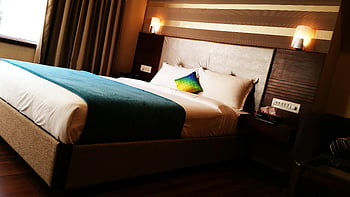 hotel room, large bed, colorful pillows, warm lighting, modern interior, blue blanket, contemporary design, bedside lamps, wooden floor, window view, decorative throw