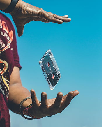 cassette tape, floating cassette, hands holding, clear blue sky, nostalgia, retro vibes, vintage music, floating object, outdoor scene, person hands, cassette tape art