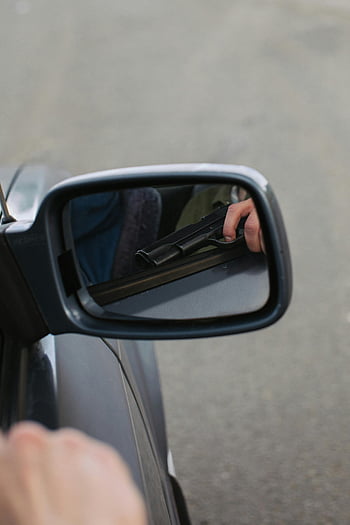 black pistol, side mirror, car reflection, handgun, outdoor view, close-up, vehicle mirror, gun reflection, mirror image, outdoor scene, hand holding gun