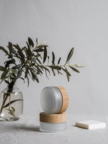cosmetic containers, gray textile, eco-friendly cosmetic jars, bamboo lids, minimalist setup, glass bottle, branch, natural beauty products, sustainable packaging, white background, decorative plant