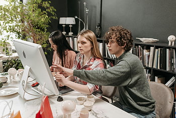woman pointing, computer screen, man in gray sweater, colleagues collaborating, stylish office space, teamwork, office environment, professional setting, computer work, office desk, workspace collaboration