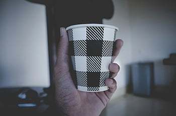 persona che tiene tazza, tazza usa e getta, modello bianco e nero, tazza con motivo geometrico, Foto interno, mano che tiene tazza, tazza di caffè, tazza a scacchi, impostazione interna, foto ravvicinata, a scacchi in bianco e nero