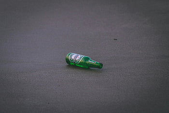 Heineken bottle, green beer bottle, asphalt surface, pollution, lone bottle, ground, environmental issue, discarded bottle, littering, urban waste, Heineken brand