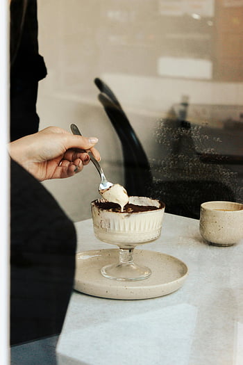 Elegant dessert, Moderne café, Cremet dessert, indbydende spisning, persons hånd, ske, Spisende atmosfære, Moderne omgivelser, Cafe -indstilling, dessertspisning, Moderne cafe -indstilling