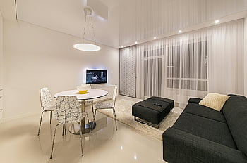 Schwarzer Stoffsofa, runder weißer Tisch, moderne Möbel, elegante Beleuchtung, Schlankes Wohnzimmer, stilvolles Interieur, zeitgemäßes Design, weiße Esszimmerstühle, Schwarze Ottomane, weiße Vorhänge, minimalistisches Dekor