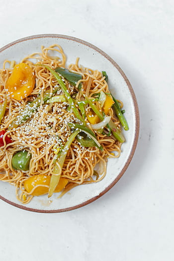 stir-fry noodles, vegetables, ceramic plate, white plate, sesame seeds, vibrant vegetables, delicious stir-fried, noodle dish, healthy meal, Asian cuisine, vegetarian dish