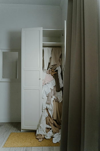 untidy closet, messy wardrobe, white wooden closet, cluttered wardrobe, overflowing clothes, dimly lit room, disorganized closet, untidy wardrobe, messy clothes, white closet, cluttered closet
