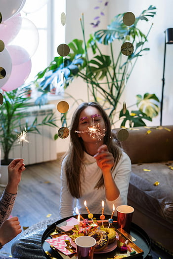 fête d'anniversaire, fête intérieure, cierges magiques, beignets, atmosphère festive, jeune femme, pull blanc, célébration intérieure, atmosphère joyeuse, beignets d'anniversaire, Décor festif
