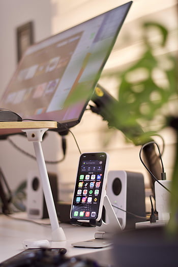 smartphone, computer, desk setup, tech-focused workspace, smartphone stand, computer screen, organized desk, speakers, tech workspace, desk accessories, plant decor