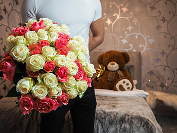 man holding flowers, bouquet of roses, romantic setting, indoor scene, teddy bear, flower arrangement, romantic flowers, man with flowers, indoor flowers, romantic bouquet, teddy bear decoration