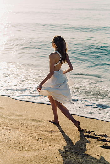 woman in white dress, beach, walking barefoot, sunlit shoreline, serene day, white dress, beach walk, barefoot walk, shoreline, serene beach, woman walking