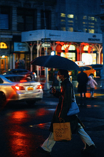face mask, umbrella, rainy street, New York City, night, shopping bag, person walking, city lights, urban scene, wet pavement, evening walk