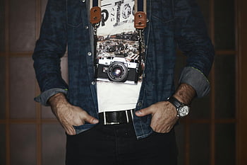 Fotografo maschio adulto, giacca di jeans, macchina fotografica d'epoca, Uomo in maglietta grigia e nera, orologio, cintura, mani in tasca, Stile casual, attrezzatura fotografica, impostazione in studio