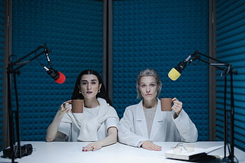 women holding mugs, podcast studio, soundproof studio, two women, microphones, blue soundproofing, studio recording, women with mugs, podcast recording, studio setup, white table