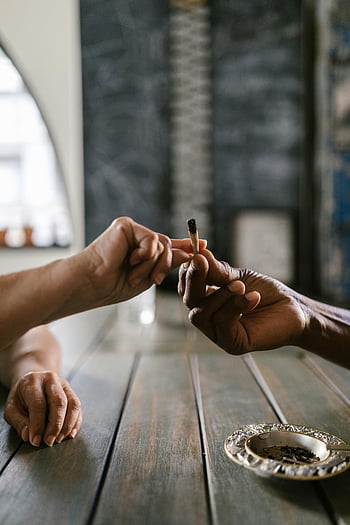marijuana joint, hands passing joint, wooden table, indoor setting, close-up photo, smoking, cannabis, ashtray, two hands, indoor scene, passing joint