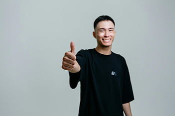 selektiver Fokus, Mann im schwarzen Hemd, Daumen hoch, Fröhlicher junger Mann, Studioeinstellung, lächelnder Mann, positive Geste, schwarzes T-Shirt, Studioportrait, männliches Model, Glücklicher Ausdruck