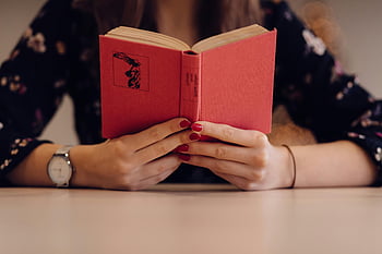 woman reading book, close-up, red book, painted nails, wristwatch, indoor setting, hands, table, floral dress, focus on hands, book cover