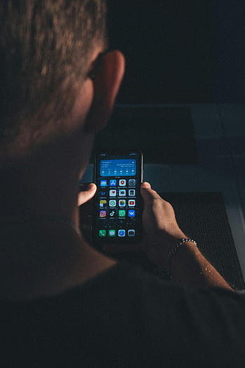 man using cellphone, close-up, smartphone, apps visible, dimly lit environment, person holding phone, mobile device, screen apps, indoor setting, technology use, individual focus