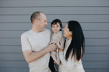 cuplu purtând copilul, portret de familie, zâmbind copilul, părinții în aer liber, peretele gri, Familia veselă, fetiță, moment de familie, Fotografie de familie în aer liber, Părinți fericiți, fericirea familiei