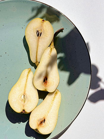 pear halves, ceramic plate, natural shadows, sliced pears, green plate, fruit photography, food art, still life, shadow cast, pear slices, plate arrangement