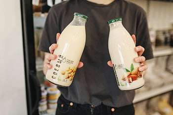 person holding bottles, almond milk, soy milk, milk substitutes, store, dairy-free milk, vegan milk, milk alternatives, glass bottles, milk products, non-dairy milk