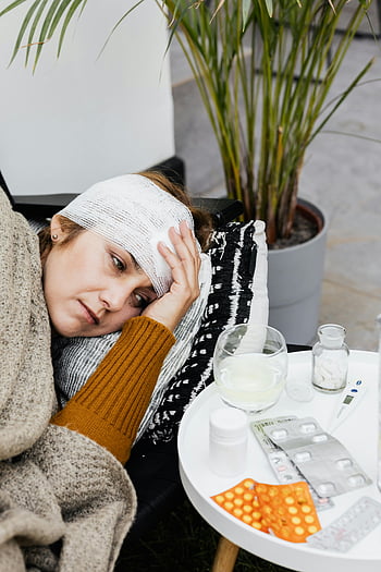woman with head bandage, feeling sick, resting, medicine table, indoors, bandage, pills, thermometer, glass of water, cozy setting, recovery