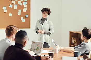 Femme portant un cardigan gris, lunettes, équipe diversifiée, réunion de bureau, graphiques sur les ordinateurs portables, discussion commerciale, cadre professionnel, travail collaboratif, salle de réunion, notes autocollantes, tasses de café