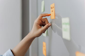 sticky note, hand, reflective surface, office setting, placing sticky note, post-it note, office environment, work space, task management, brainstorming, planning