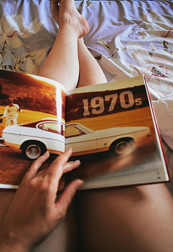 person holder bog, Retro Magazine, 1970'erne klassiske biler, indendørs afslapning, Nærbillede, Vintage bilbog, skødelæsning, indendørs fritid, bil entusiast, Klassisk bilmagasin, 1970'erne biler