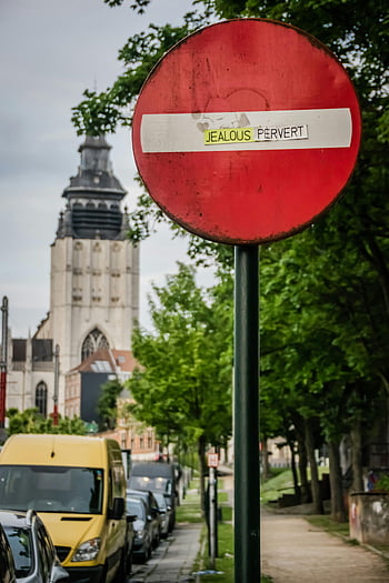 red traffic sign, graffiti, urban setting, church, parked cars, metal signage post, street scene, outdoor photography, cityscape, street sign, urban environment
