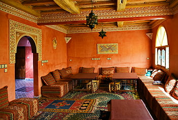 Marokkaans interieur, Rode woonkamer, traditionele inrichting, levendige patronen, Gezellige zitplaatsen, zonovergoten kamer, Marokkaans ontwerp, cultureel decor, sierlijke plafond, patroon tapijten, houten tafels