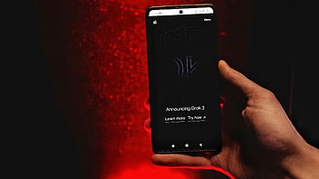 hand holding smartphone, Grok 3 announcement, smartphone display, red background, announcing Grok 3, learn more, try now, black screen, digital announcement, technology news, product launch