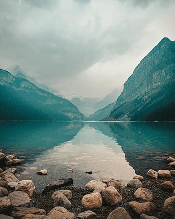 Lake Louise, mountain scenery, panoramic view, mountain reflections, overcast sky, natural landscape, calm water, rocky shore, alpine lake, Canadian Rockies, serene environment