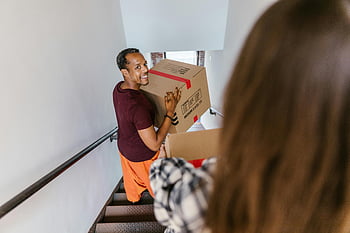 man carrying box, going down stairs, indoor staircase, moving box, smiling man, carrying box, indoor scene, man with box, staircase indoors, moving day, adult man