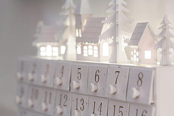 white calendar, white surface, minimalist advent calendar, illuminated houses, winter decor, festive ambiance, white houses, white trees, white numbers, white festive decor, white advent calendar