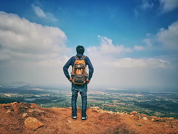 Mann, blaues Hemd, blaue Jeans, orange Rucksack, Gebirgsklippe, szenische Ansicht, Stadt, Dorf, blauer Himmel, weiße Wolken, weitläufige Ansicht, strahlender Himmel