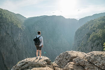 Muž s batohem, stojící na útesu, horský kaňon, slunečný den, pohled, venkovní dobrodružství, přírodní krajina, turista, cestovní fotografie, dobrodružné cestování, batohem