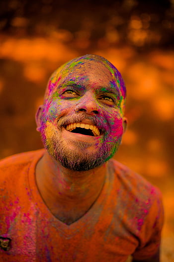 Holi festival, man with paint, vibrant colors, orange shirt, smiling man, traditional celebration, India, colorful face, festival joy, cultural event, happy celebration