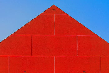 red building, modern architecture, triangular facade, clear blue sky, red blocks, close-up view, contemporary design, geometric structure, minimalist architecture, vibrant red, architectural photography