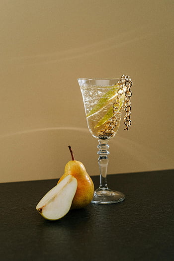 pear cocktail, crystal glass, gold chain, classy occasions, sophisticated drink, pear garnish, elegant beverage, cocktail drink, pear slice, black surface, beige background