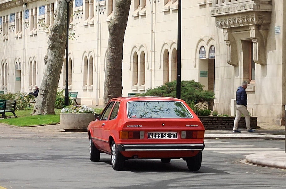 VW Scirocco, červené auto, Historické auto, ulice, zaparkované auto, muž chůze, stavební fasáda, stromy, lavičky, poznávací značka, městské scény