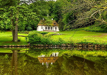 white and brown house, surrounded by trees, picturesque cottage, thatched roof, serene lake, lush greenery, reflection, tranquil scene, natural setting, countryside charm, peaceful environment
