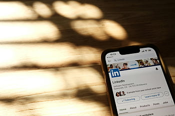 LinkedIn, smartphone screen, close-up, LinkedIn profile, wooden table, shadows, mobile device, professional networking, app interface, social media, technology