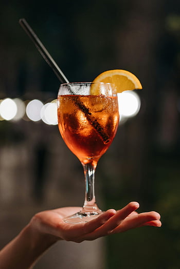 aperol spritz, koktejl, plátky pomeranče, čiré sklenice na víno, ruka hospodářství, rozmazané noční pozadí, detail, napít se, nápoj, večer, občerstvení