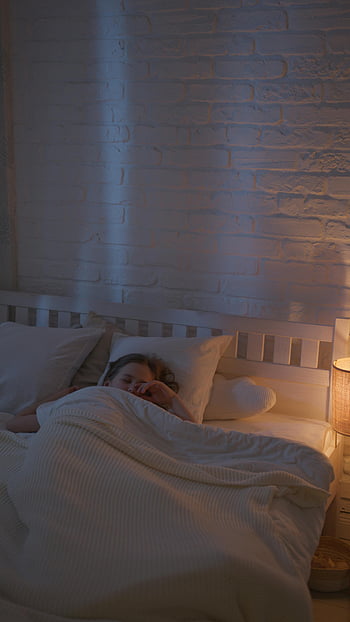 child sleeping, cozy blanket, softly lit bedroom, warm bedroom, white brick wall, comfortable bed, peaceful sleep, nighttime scene, soft lighting, child in bed, cozy atmosphere