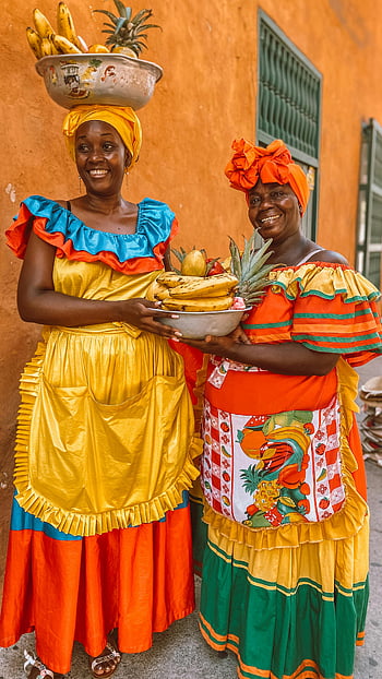 smiling women, bowls of fruit, vibrant traditional attire, holding fruit, Cartagena, Colombia, colorful dresses, tropical fruit, cultural attire, street scene, local culture