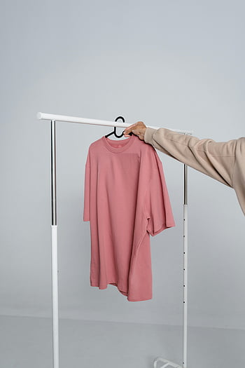 rosa T-Shirt, Person, die Hemd hält, Kleiderständer, Mode-Design, Modelle, Langarm-Shirt, Aufhänger, minimalistischer Hintergrund, Freizeitkleidung, Kleidungsdisplay, Modefotografie