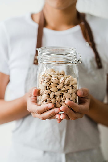 pistachio nuts, clear glass jar, healthy eating, close-up photo, hands holding jar, shelled pistachios, pistachio jar, pistachio snack, pistachio health benefits, pistachio container, pistachio storage