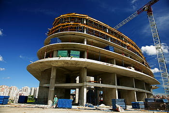 unfertiges graues Betongebäude, kreisförmiges Gebäude, im Bau, Kran, klarer blauer Himmel, Flachwinkelansicht, Baustelle, Hochbau, konkrete Struktur, blauer Himmel, Baukran