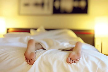 person lying on bed, white blanket, relaxing, feet under sheets, serenity, bedroom, comfort, cozy, rest, sleep, hotel room